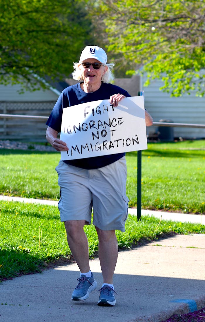 Senior adult holding sign that reads 'Fight Ignorance Not Immigration' during a protest.